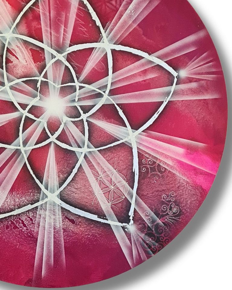 Detaillierte Ansicht eines künstlerisch gestalteten runden Objekts mit einem weißen Venusblumen-Motiv vor einem rot-pinken Hintergrund mit leuchtenden Strahlen und filigranen Verzierungen.